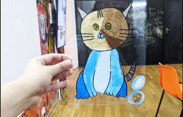 Hand holding perspex sheet with illustration of a cat on it.