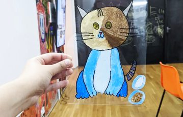 Hand holding perspex sheet with illustration of a cat on it.