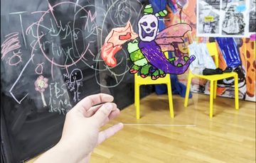 Hand holding perspex sheet with illustration on it, in front of a room.