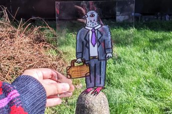 Hand holding a perspex sheet with an illustration of a pigeon in a suit, holding a bag.