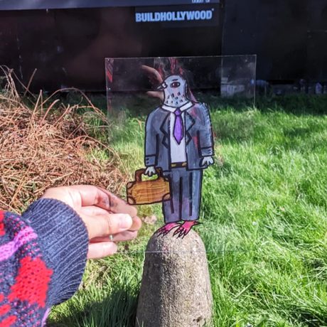 Hand holding a perspex sheet with an illustration of a pigeon in a suit, holding a bag.