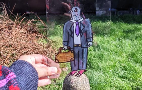 Hand holding a perspex sheet with an illustration of a pigeon in a suit, holding a bag.