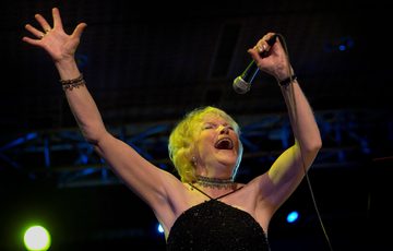 Jal Wiseman singing into a microphone with her hands in the air.