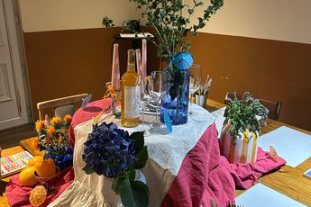 A table is set up with flowers, vases and paint brushes and paper.