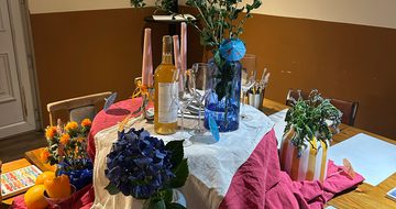 A table is set up with flowers, vases and paint brushes and paper.