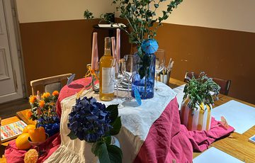 A table is set up with flowers, vases and paint brushes and paper.