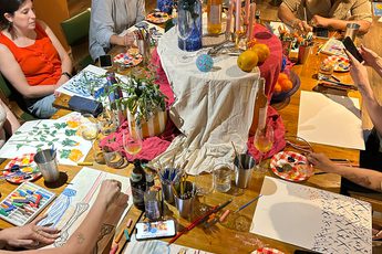 A group of people are painting at a table decorated with flowers and vases.