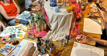 A group of people are painting at a table decorated with flowers and vases.