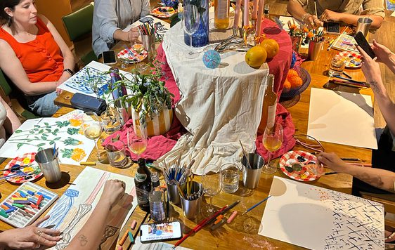 A group of people are painting at a table decorated with flowers and vases.