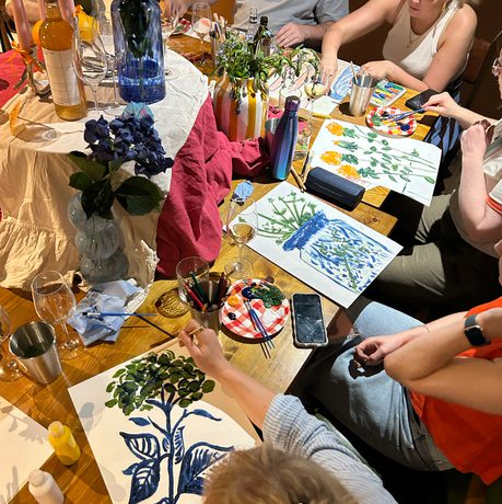 A group of people are painting at a table decorated with flowers and vases.