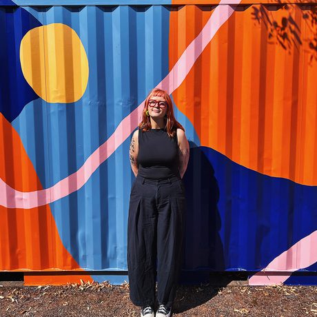 A lady standing in front of a colourful geometric painted background.