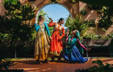 A group of three performers posing in front of an arched window and trees.