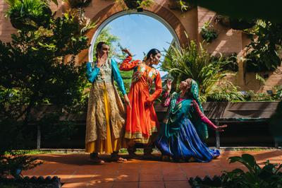 A group of three performers posing in front of an arched window and trees.