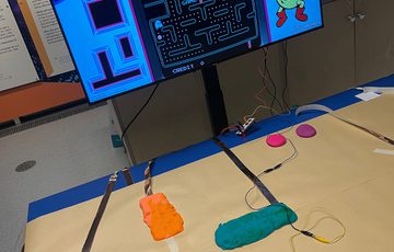 Table with colourful dough connected a cable to a screen with a computer game on it.