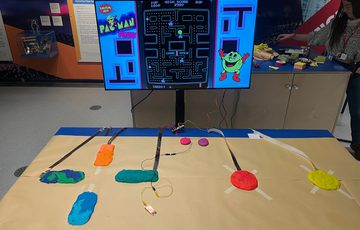 Table with colourful dough connected a cable to a screen with a computer game on it.
