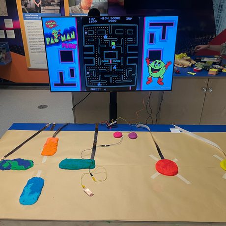 Table with colourful dough connected a cable to a screen with a computer game on it.