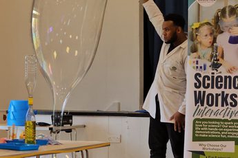 A person holding a hoop in the air, a large bubble is coming from floor to the hoop.