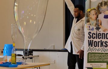 A person holding a hoop in the air, a large bubble is coming from floor to the hoop.
