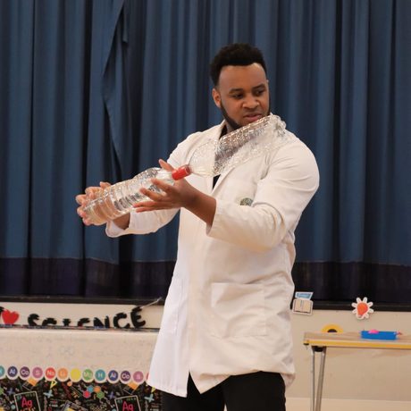 A person in a lab coat holding two joined plastic bottles as part of a science experiment.