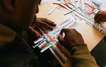 A person leaving over and weaving paper on a table.