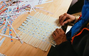 A table with slices of paper being woven by a person.