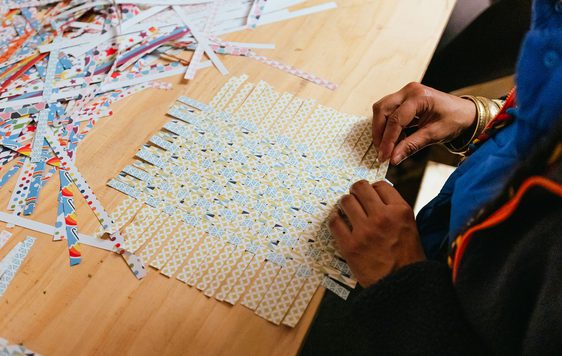 A table with slices of paper being woven by a person.