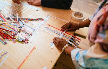 A person weaving paper on a table.