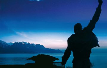 Picture of a silhouette of a man holding his arms up, against an ocean and mountain landscape after sunset