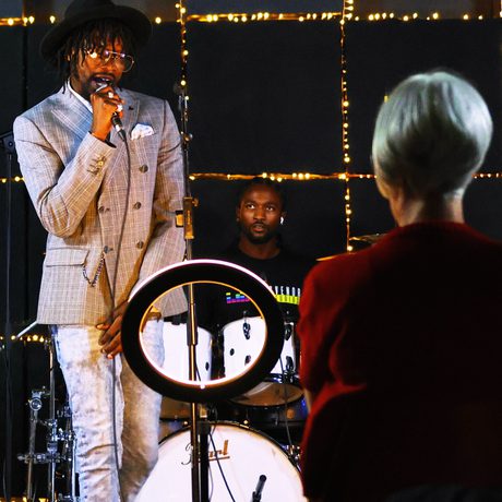 A person standing in a room with a microphone, in front of them is a person and ring light.