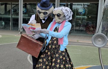 Two people dressed as alien Roswell characters checking a map in the Science Garden at Thinktank.