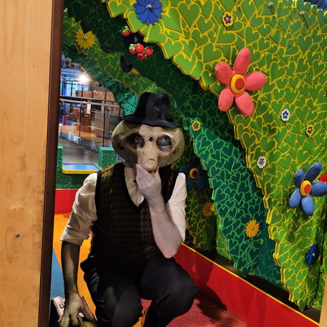 One person dressed as alien Roswell posing under a fake tree display.
