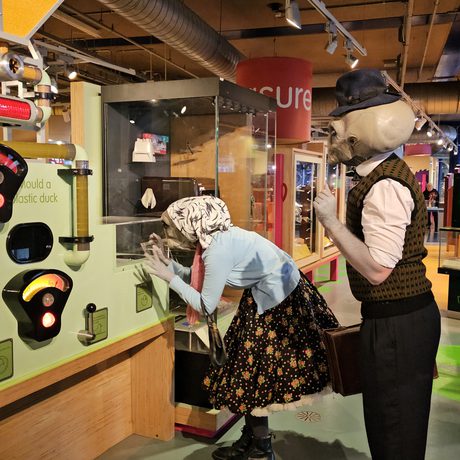 Two people dressed as alien Roswell characters looking at display.