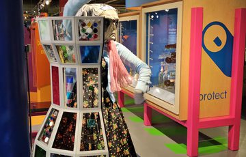 A person dressed as alien Roswell character dancing by a bottle shaped interactive.