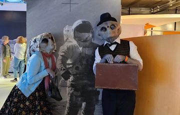 Two people dressed as alien Roswell characters  posing with a photo graphic of an astronaut.