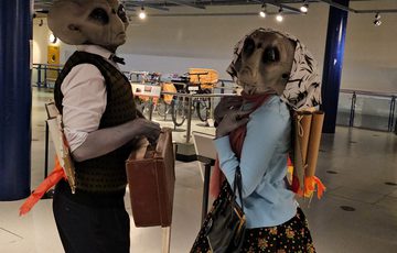 Two people dressed as alien Roswell characters posing with cardboard backpacks.