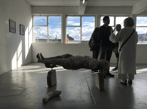 Three people in a gallery stand near what appears to be a model of a person that is floating in mid-air.