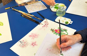 Close up of people painting on paper at a table.