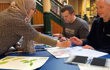 Two adults at a table being guided by another adult in a painting activity.