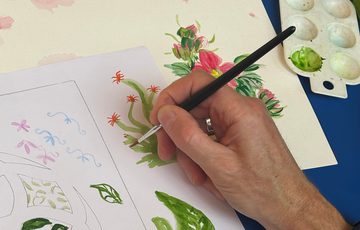 Close up of a hand painting flowers and leaves on paper.
