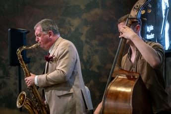 Two musicians performing, one is playing a saxophone and the other a cello.