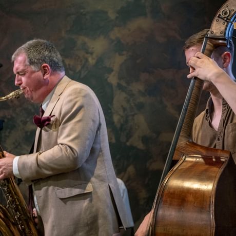 Two musicians performing, one is playing a saxophone and the other a cello.