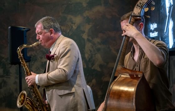 Two musicians performing, one is playing a saxophone and the other a cello.