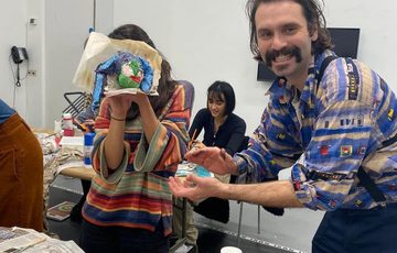 An artist with a person who is holding their piece of art to cover their face.