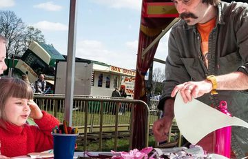 An artist at a table full of art supplies with a child taking part in the craft.