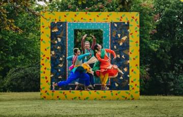 Three dancers performing outside with square and rectangular frames behind them as they jump in the air.