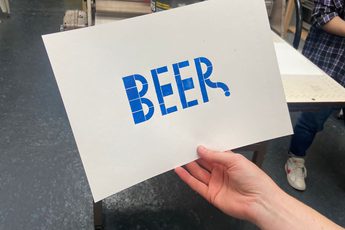 A hand holding a paper with 'Beer' printed onto it in blue print.