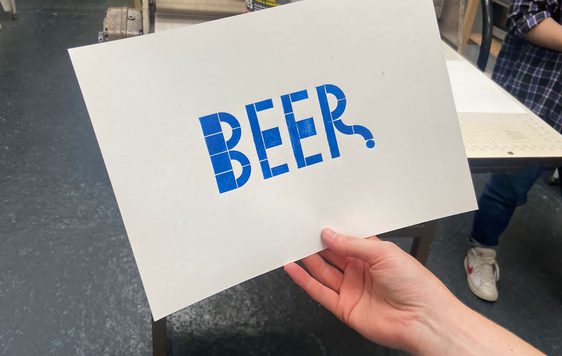 A hand holding a paper with 'Beer' printed onto it in blue print.