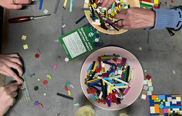 A view of a table from above with pots of plastic brick pieces and people's hand making designs.