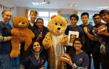 A group of people with a teddy bear mascot in the centre. The people are holding large fake teeth, a teddy bear and wearing stethoscopes.