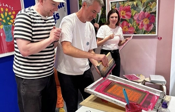 Joe Lycett watching a person screen printing.